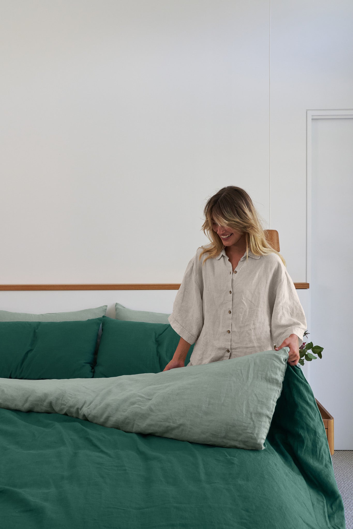 Model kneeling on her bed with French flax linen double sided quilt cover in sage/jade