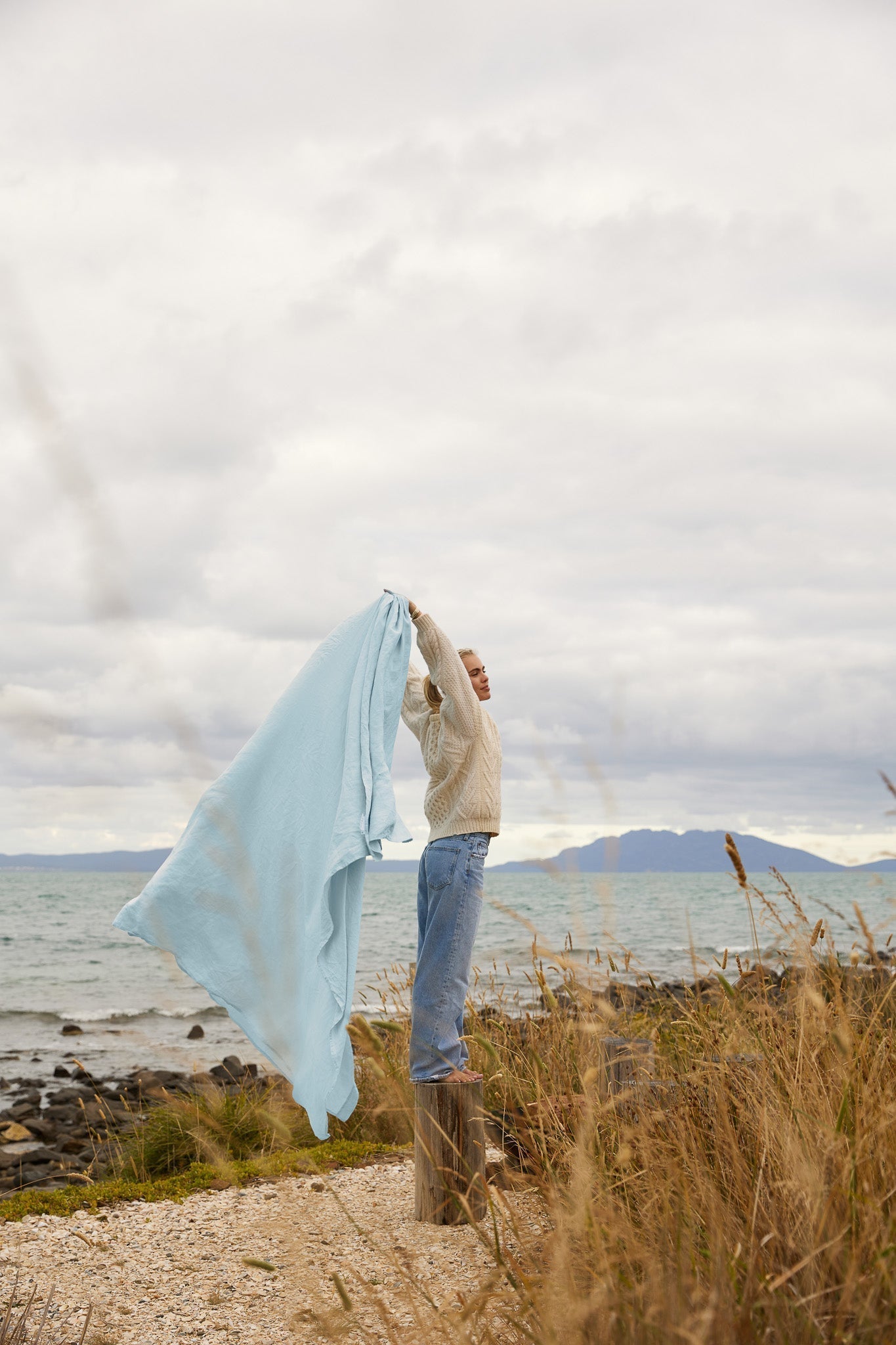 Sky Blue flat sheet being held up by a model by the sea 